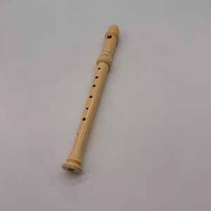以下が含まれることがあります： クリーム色のリコーダー、木管楽器が白い背景に表示されています。リコーダーにはマウスピース、指穴、フレアエンドがあります。楽器はプラスチックまたは木材で作られています。