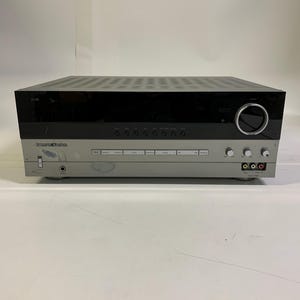 以下が含まれることがあります： シルバーとブラックのハーマンカードンレシーバー。レシーバーは黒い上部とシルバーの下部があり、いくつかのボタンとノブが付いています。フロントパネルにはハーマンカードンのロゴと、さまざまな入出力ポートがあります。