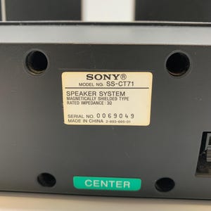 May include: A black Sony speaker system, model SS-CT71, featuring a center channel label. The back panel includes a white identification sticker with technical specifications, including a rated impedance of 3 ohms, and a green label marked CENTER.