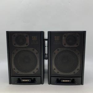 May include: A pair of black Sony speakers featuring a rectangular design with a mesh front grille. Each speaker unit displays the word SAT near the top and the Sony brand name printed on a small rectangular plate at the bottom center.
