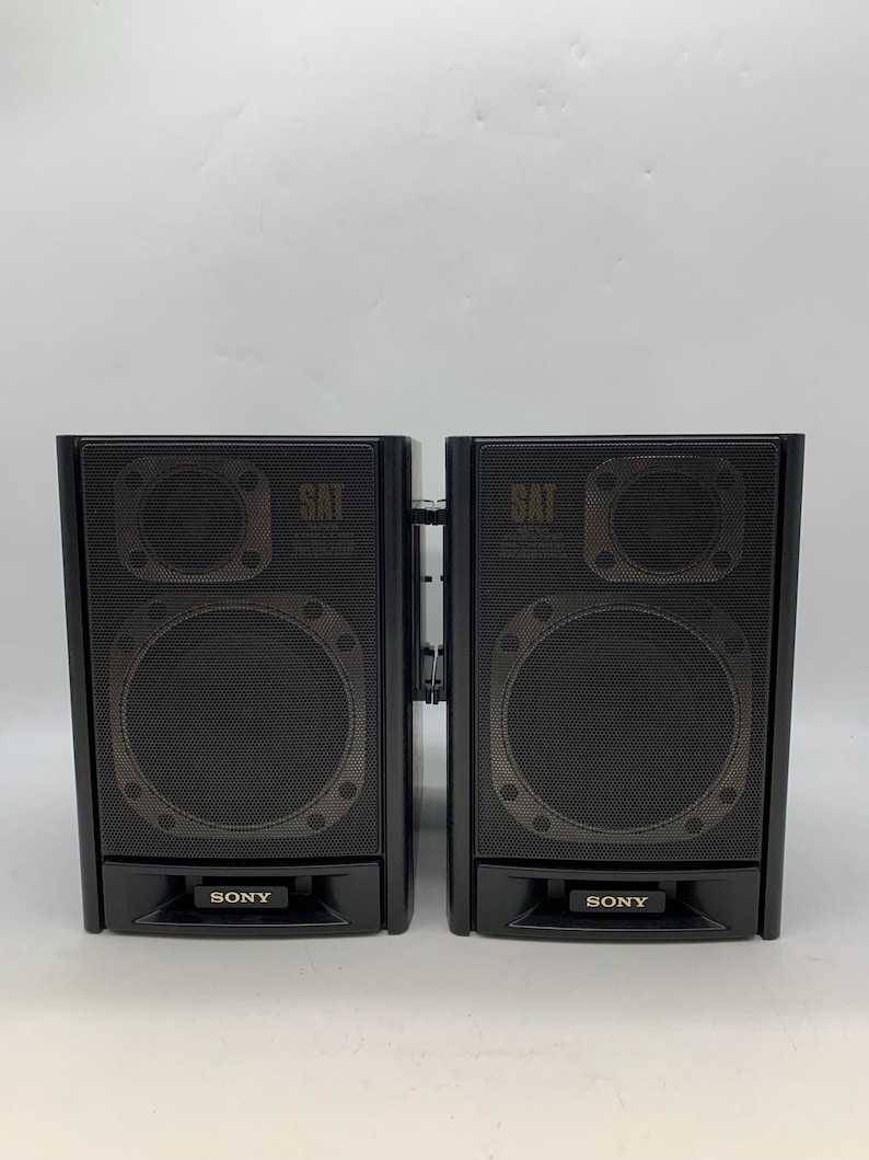 May include: A pair of black Sony speakers featuring a rectangular design with a mesh front grille. Each speaker unit displays the word SAT near the top and the Sony brand name printed on a small rectangular plate at the bottom center.