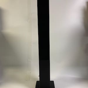 Op de afbeelding: Een hoge, zwarte, rechthoekige displaystandaard. De standaard heeft een vierkante basis en een lange, verticale behuizing. De standaard is gemaakt van een matzwart materiaal en is ontworpen om een display te bevatten.