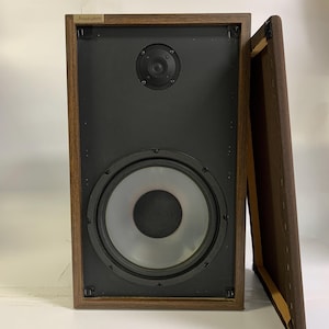 May include: Acoustisphere speaker with a dark wood frame and a black speaker face. The speaker has a large central woofer and a smaller tweeter. The speaker's brown fabric cover is partially removed. The brand name "Acoustisphere" is visible.