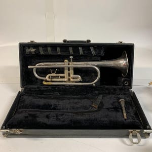 May include: A silver-colored flugelhorn rests inside an open black case with a black velvet interior. The case also contains a mouthpiece and a black strap. The flugelhorn is a brass instrument with valves and a bell.