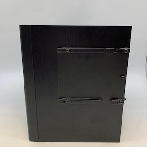 May include: A rectangular black wooden frame with a smooth finish, featuring a central black plastic insert secured by four small clips on the front surface. The frame has a solid, dark appearance with a clean, minimalist design and visible hardware.
