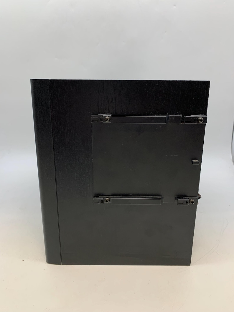 May include: A rectangular black wooden frame with a smooth finish, featuring a central black plastic insert secured by four small clips on the front surface. The frame has a solid, dark appearance with a clean, minimalist design and visible hardware.