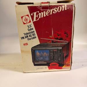 K&ouml;nnte beinhalten: Ein Emerson 5,5" Farbfernseher in der Originalverpackung. Die Box ist rot und wei&szlig; mit dem Emerson-Logo und Produktinformationen. Der tragbare Fernseher hat ein schwarzes Geh&auml;use und einen kleinen Bildschirm, der eine Stadtlandschaft zeigt.