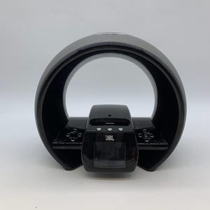May include: Black JBL speaker system with a circular design and a rectangular base. The speaker has a textured surface on the top and a display screen on the front. The JBL logo is visible on the front.