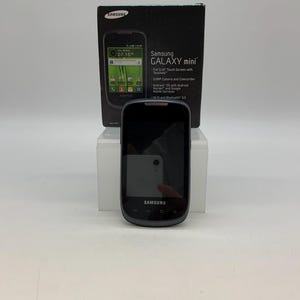 Könnte beinhalten: Ein schwarzes Samsung Galaxy Mini Smartphone mit 3,14-Zoll-Touchscreen, 3,0-MP-Kamera und Android OS. Das Telefon wird vor seiner originalen schwarzen Box präsentiert, die ebenfalls das Bild und die Spezifikationen des Telefons zeigt.