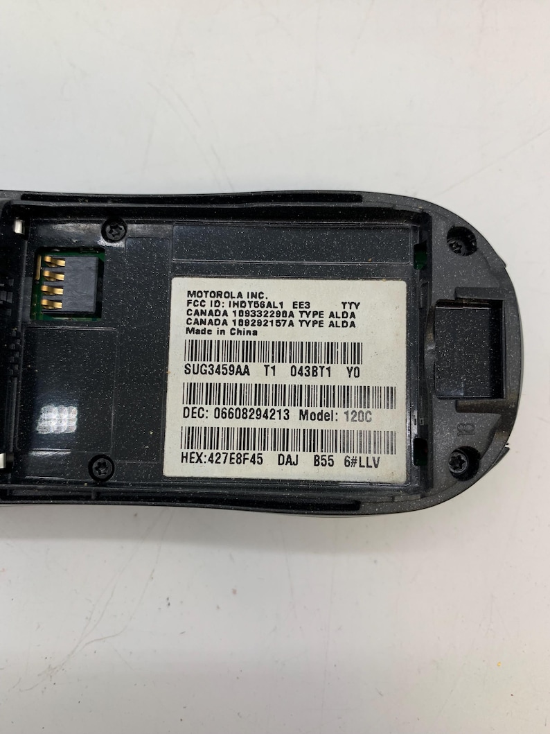 May include: A close-up of the inside of a black Motorola 120C phone. The phone's internal components are visible, including a circuit board and a label with technical specifications. The label includes the FCC ID, model number, and other regulatory information.