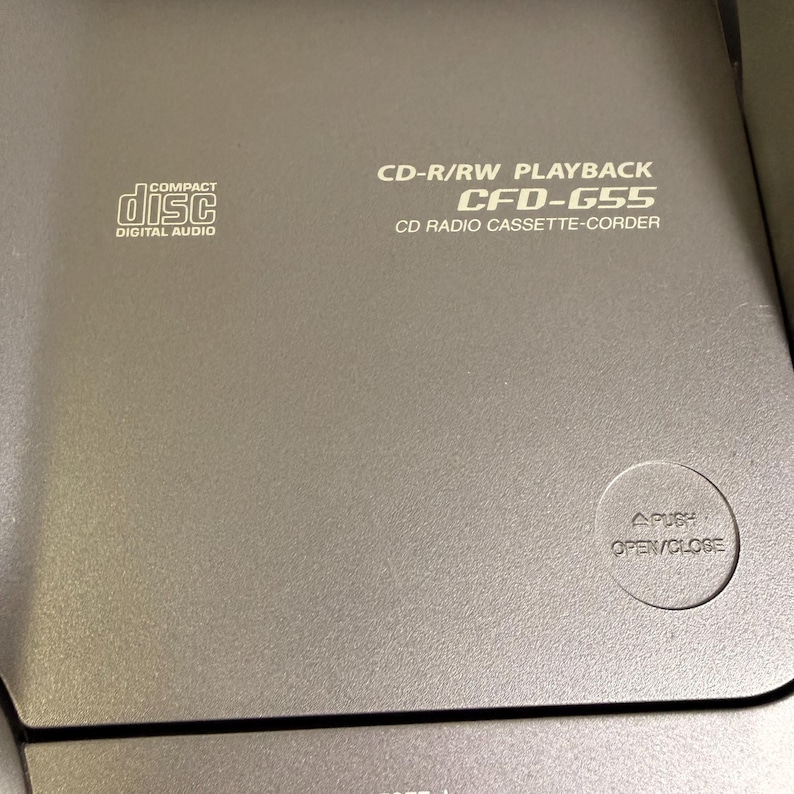 K&ouml;nnte beinhalten: Ein grauer CD-Radio-Kassettenrekorder mit dem Text CD-R/RW PLAYBACK CFD-G55 CD RADIO CASSETTE-CORDER auf der Oberseite. Das Ger&auml;t verf&uuml;gt &uuml;ber ein Compact Disc Digital Audio-Logo und eine runde Taste mit der Aufschrift PUSH OPEN/CLOSE.