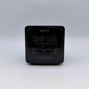 May include: Black Sony Dream Machine digital clock radio. The radio has an AM/FM tuner, a digital display, and the text "DREAM MACHINE". The radio has a black exterior.