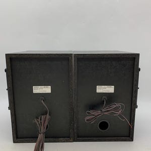 May include: Two black Sony SS-H65 speaker systems shown from the rear. Each unit features a rectangular wooden cabinet, a central circular port, and a white identification label with the text SONY SS-H65 SPEAKER SYSTEM, along with serial numbers.