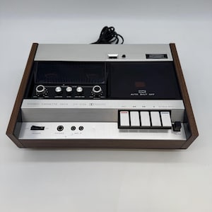 Può includere: Un lettore di cassette stereo vintage con una facciata argentata, finiture in legno scuro e pulsanti neri. Il lettore presenta un interruttore di alimentazione, un jack per cuffie e varie manopole di controllo. Il testo "Superscope" è visibile e "CD-302A" è stampato.