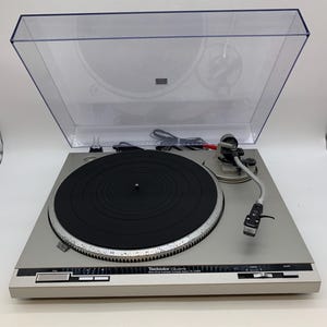 May include: Silver Technics SL-Q303 turntable with a black platter and a clear dust cover. The turntable features a tonearm, control buttons, and the Technics logo.