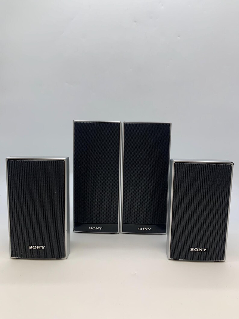 May include: Four rectangular Sony speakers with black mesh grilles and silver frames. Two speakers are taller and positioned in the center, while two shorter speakers are placed on the outer sides. Each speaker features the Sony logo in white text.