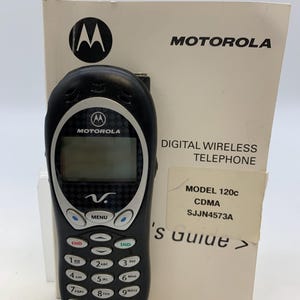 May include: Black Motorola 120c CDMA digital wireless telephone with a matching instruction manual. The phone has a black keypad with white numbers and a small LCD screen. The manual displays the Motorola logo.