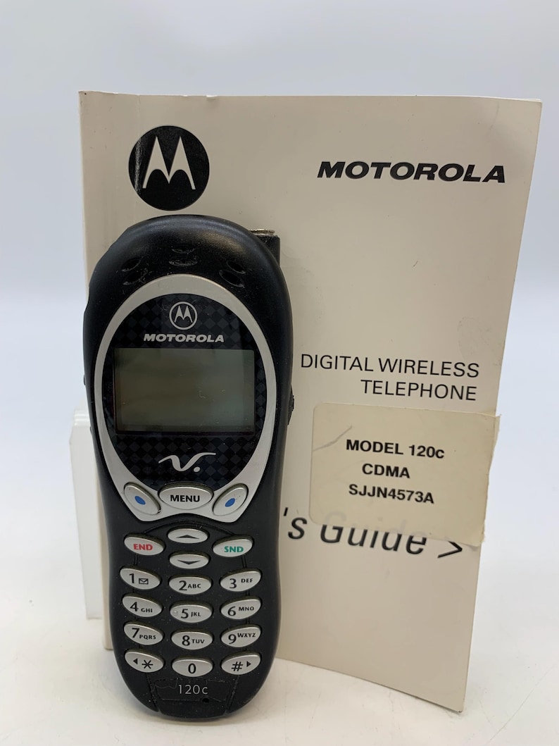 May include: Black Motorola 120c CDMA digital wireless telephone with a matching instruction manual. The phone has a black keypad with white numbers and a small LCD screen. The manual displays the Motorola logo.
