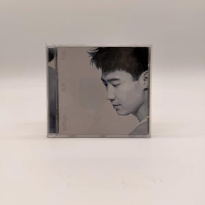 May include: A CD case featuring a grayscale image of a man in profile. The CD case has the text "leon" and "perhaps..." printed on it. The CD case is in a clear plastic case.