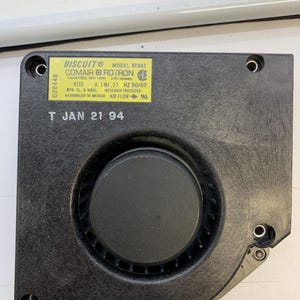 May include: A black Biscuit model BT2A1 fan with a central circular component and a yellow label. The label includes text such as "COMAIR ROTRON" and "ASSEMBLED IN MEXICO". The date "T JAN 21 94" is also visible.