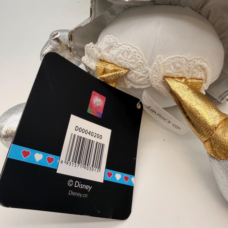 May include: A plush toy with a white body, gold horn, and silver accents. The toy has a tag with the Disney logo and a barcode. The tag also has the text "Disney.cn".