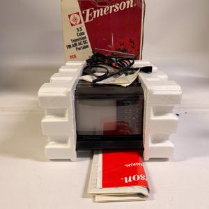 K&ouml;nnte beinhalten: Ein Vintage Emerson 5,5-Zoll-Farbfernseher, FM/AM AC/DC tragbar, in Originalverpackung. Der Fernseher ist schwarz mit einem silbernen Bildschirm, und die Box ist rot und wei&szlig;. Das Handbuch ist rot und wei&szlig;.
