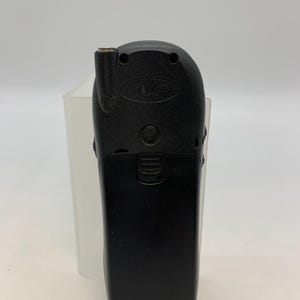May include: A black vintage mobile phone with a rounded top and a rectangular bottom. The phone has a small antenna and several buttons. The phone is set against a white background.