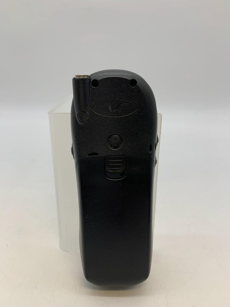 May include: A black vintage mobile phone with a rounded top and a rectangular bottom. The phone has a small antenna and several buttons. The phone is set against a white background.