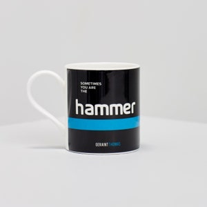 Könnte beinhalten: Weiße Keramik-Tasse mit schwarzem Band, das den weißen Text "Sometimes You Are The Hammer" mit blauem Streifen trägt. Der Name "Geraint Thomas" ist unten aufgedruckt. Die Tasse hat einen weißen Henkel.
