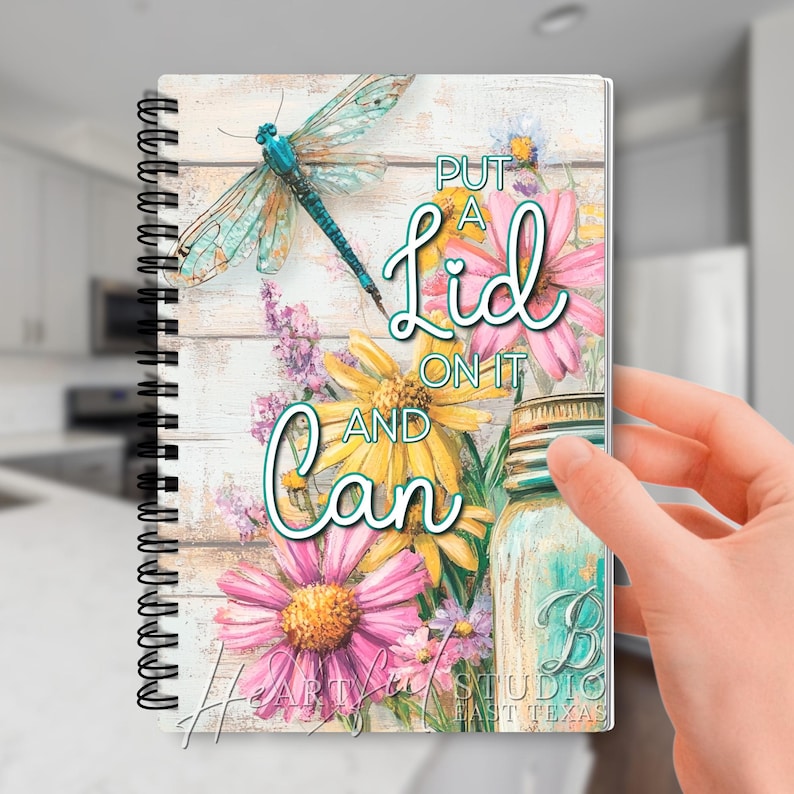 K&ouml;nnte beinhalten: Spiralgebundenes Notizbuch mit floralem Design mit einer Libelle, G&auml;nsebl&uuml;mchen und dem Text "Put a Lid on it and Can". Das Notizbuch hat einen rustikalen, verwitterten Holzgrund mit einem teal- und rosa Farbschema.