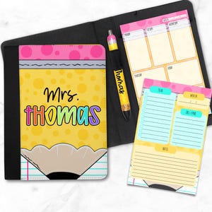 Könnte beinhalten: Ein Schreibwarenset zum Thema Lehrer, mit einem notizbuchförmigen Bleistift-Cover mit bunten Buchstaben "Mrs. THOMAS". Enthält einen passenden Stift, Notizblock und Wochenplaner, alle mit rosa und gelben Akzenten. Das Set ist für die Organisation gedacht.