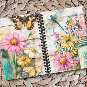 K&ouml;nnte beinhalten: Spiralgebundenes Notizbuch mit Blumen- und Schmetterlingsdesign. Das Notizbuch zeigt rosa, gelbe und wei&szlig;e Blumen, Schmetterlinge und eine Libelle. Der Text "Put a Lid on it and Can" steht auf der rechten Seite.