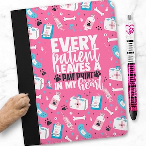 Può includere: Un quaderno rosa con dorso nero e penna abbinata. Il quaderno presenta un motivo ripetuto di forniture mediche e impronte di zampe. Il testo sul quaderno recita: "Ogni paziente lascia un'impronta di zampa nel mio cuore."