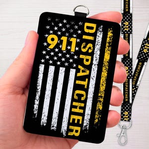 May include: A black 911 dispatcher badge with a distressed American flag design. The badge features the text "911 DISPATCHER" in yellow. A matching lanyard is also visible.
