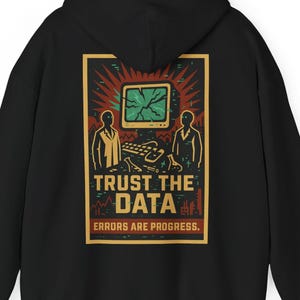 Può includere: Felpa con cappuccio nera con grafica sul retro. Il design include un computer retrò, due figure e il testo "TRUST THE DATA. ERRORS ARE PROGRESS." La grafica è nei colori rosso, verde e giallo.