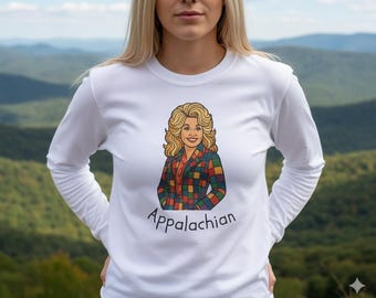 Op de afbeelding: Wit shirt met lange mouwen met een kleurrijke illustratie van een vrouw in een geruite jas. Het woord "Appalachian" staat in zwart schrift eronder. Het shirt is gemaakt van een zacht materiaal.