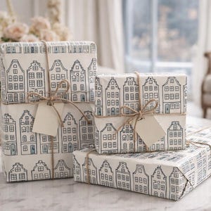 May include: Four wrapped gifts on a marble table. The gifts are wrapped in white paper with a repeating black and blue house pattern. Each gift is tied with twine and has a blank tag. A vase of flowers is in the background.