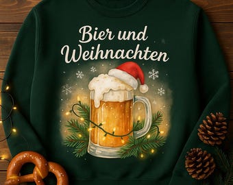 May include: Dark green sweatshirt with the text "Bier und Weihnachten" above a beer stein wearing a Santa hat. The beer stein is surrounded by Christmas lights and pine branches. A pretzel and pine cones are in the foreground.