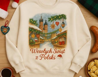 Może przedstawiać: Kremowa bluza z nadrukiem przedstawiającym zimowy jarmark z śniegiem, budynkami i dekoracjami. Tekst "Wesołych Świąt z Polski" jest wyświetlany na brązowo. Zawiera również grafikę czapki Świętego Mikołaja.