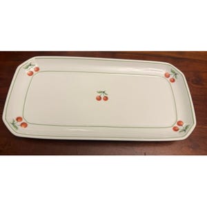 May include: A rectangular white ceramic serving platter featuring a thin green border line and small red cherry illustrations with green leaves. The cherries are positioned at each of the four corners and a single pair is centered on the platter.