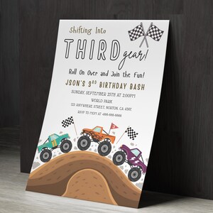 May include: A white invitation card with the text "Shifting Into THIRD gear!" and "JASON'S 3rd BIRTHDAY BASH". The card features illustrations of monster trucks in teal, orange, and purple, racing on a dirt track, with checkered flags.