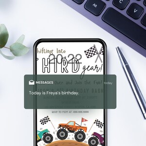 May include: A smartphone displays a birthday invitation with monster trucks and checkered flags. The text reads "Shifting Into HTRD gear!" and "Today is Freya's birthday." A pen and keyboard are in the background.