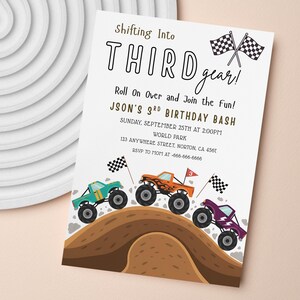 May include: A white invitation card with the text "Shifting Into THIRD gear!" and "JASON'S 3RD BIRTHDAY BASH". The card features illustrations of monster trucks in teal, orange, and purple, racing over a brown hill, with checkered flags.