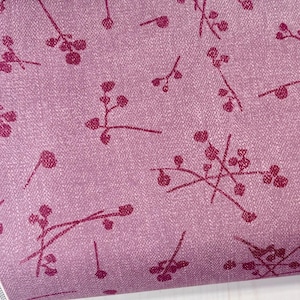 May include: A roll of fabric with a pinkish-purple background and a repeating pattern of dark pink floral sprigs. The fabric has a textured appearance. The selvage edge features text including "Dusk Fusion" and "Katarina Roccella."
