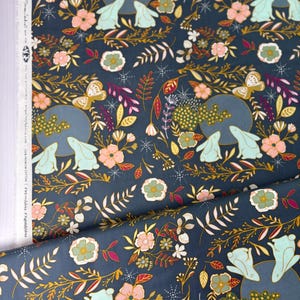 May include: Dark blue fabric with a repeating pattern of rabbits, butterflies, flowers, and foliage in shades of pink, green, gold, and white. The design includes a moon-like circle with two rabbits. The fabric is likely cotton.