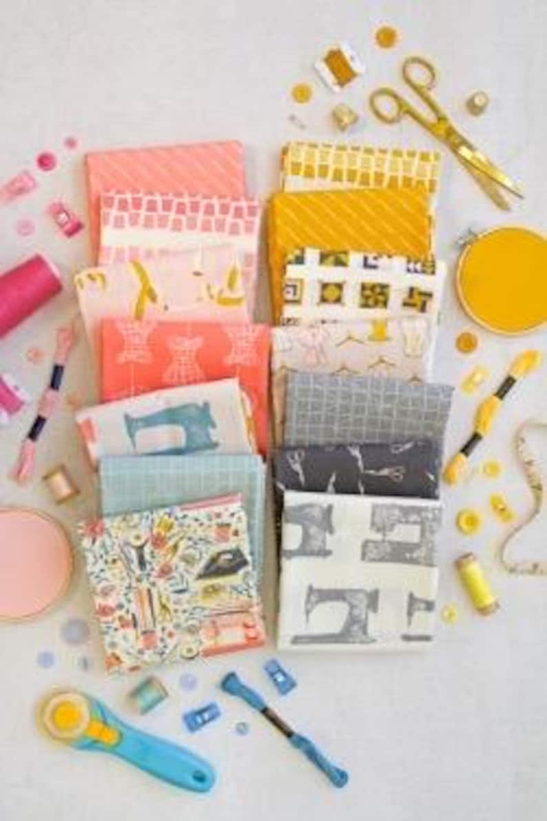 May include: An overhead shot of a collection of folded fabric squares in various colors and patterns, including pink, yellow, and blue. Sewing notions like scissors, thread, and buttons are scattered around the fabric, suggesting a crafting theme.