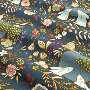 May include: Dark teal fabric with a floral and bunny pattern. The design features pink, white, and yellow flowers, along with light blue bunnies and gold-colored vines and leaves. The fabric has a soft, textured appearance.