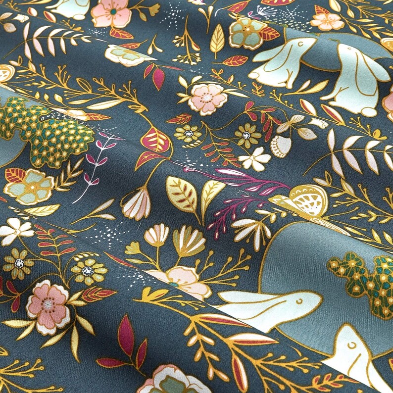 May include: Dark teal fabric with a floral and bunny pattern. The design features pink, white, and yellow flowers, along with light blue bunnies and gold-colored vines and leaves. The fabric has a soft, textured appearance.