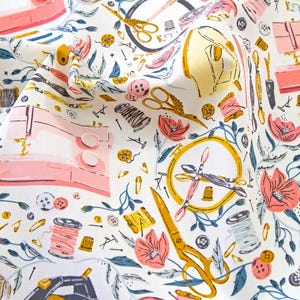 May include: White fabric with a repeating pattern of sewing machines, scissors, spools of thread, buttons, and floral elements in pink, yellow, and blue. The design evokes a craft or hobby theme.
