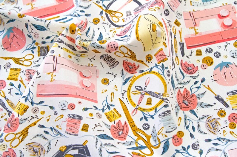 May include: White fabric with a repeating pattern of sewing machines, scissors, spools of thread, buttons, and floral elements in pink, yellow, and blue. The design evokes a craft or hobby theme.